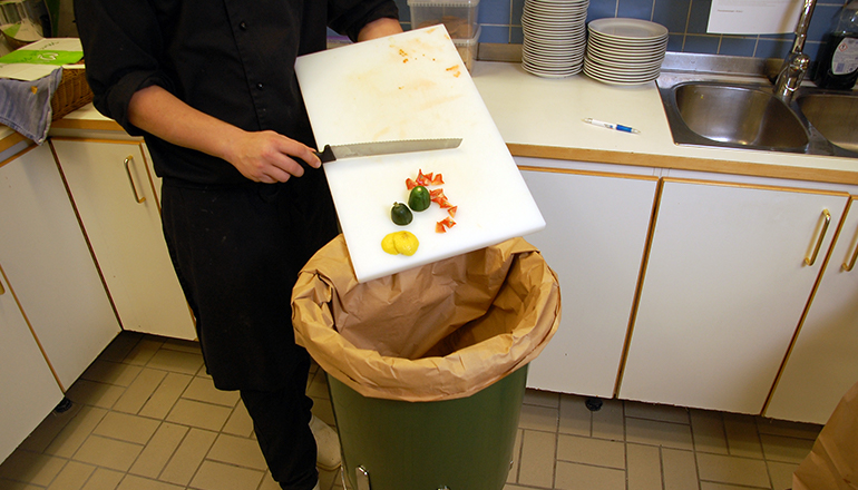 Skärbräda med grönsaksrester töms ned i en säck
