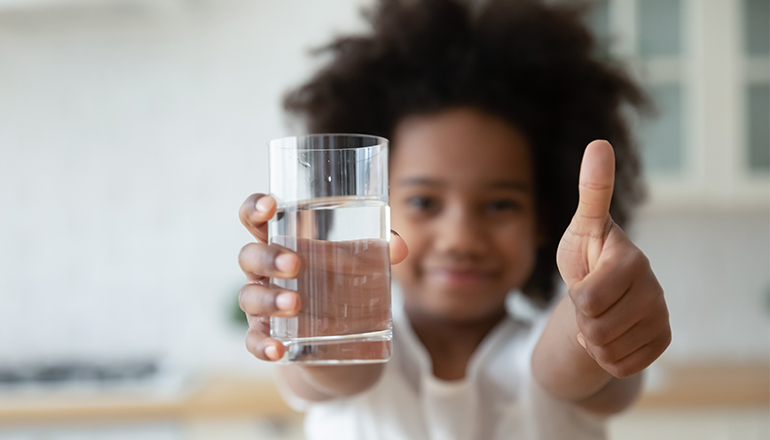 Flicka gör tummen upp för vatten i ett glas